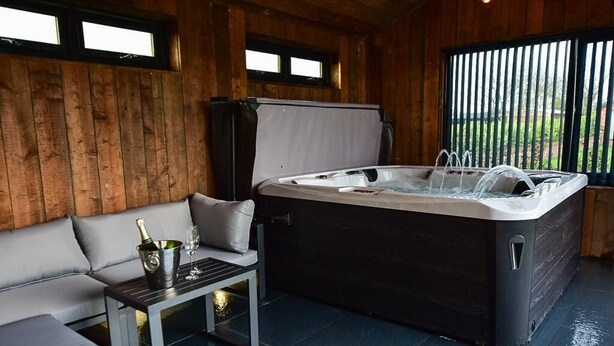 A wooden room with a hot tub, a sofa, and a table with a bottle and glasses. - Private Lodge With Hot tub in Blackpool (Blackpool)