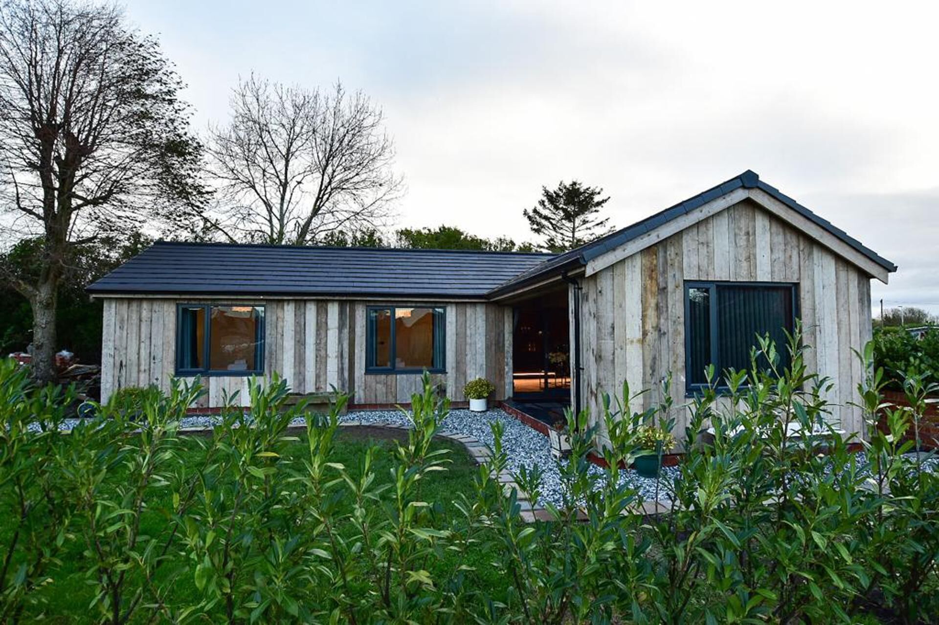 Une maison moderne en bois, dotée d’un toit à pente, de grandes fenêtres et d’un porche abrité.
