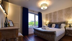 A bedroom with a large bed, a bedside table, a nightstand, a window with curtains, and a chandelier. - Private Lodge With Hot tub in Blackpool (Blackpool)