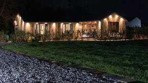 A modern house with a well-lit exterior, a paved driveway, and a grassy lawn. - Private Lodge With Hot tub in Blackpool (Blackpool)