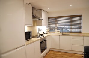 A modern kitchen with white cabinets, a microwave, a stove, and a window with blinds.