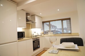 A modern kitchen with white cabinets, a microwave, an oven, and a dining area with a table set for two. - in the charming Old Town one minute walk from shops, cafes, pubs & large park. (Hemel Hempstead)
