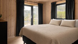 Un dormitorio con una cama grande, paredes de madera y dos ventanas con cortinas.