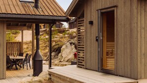 Una cabaña de madera con una terraza, una mesa con sillas y una chimenea.