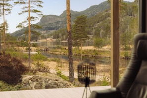 A room with a view of a lake surrounded by trees and mountains.
