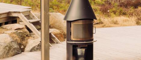 A wood-burning stove under a wooden structure with a view of a forested area.