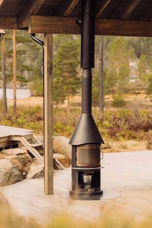 A wood-burning stove under a wooden structure with a view of a forested area.