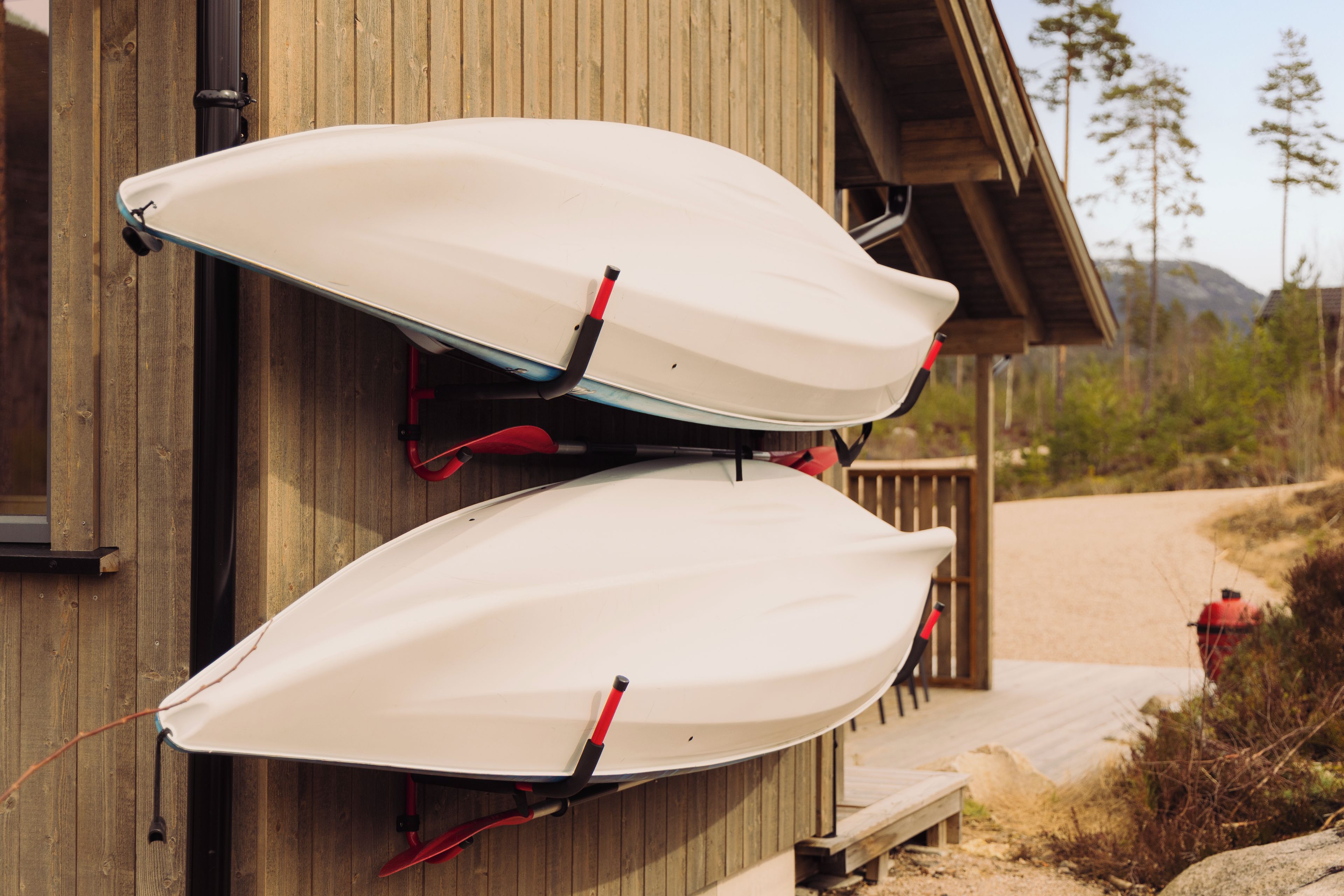 Deux kayaks blancs sont fixés à un mur en bois à l’aide de sangles rouges.