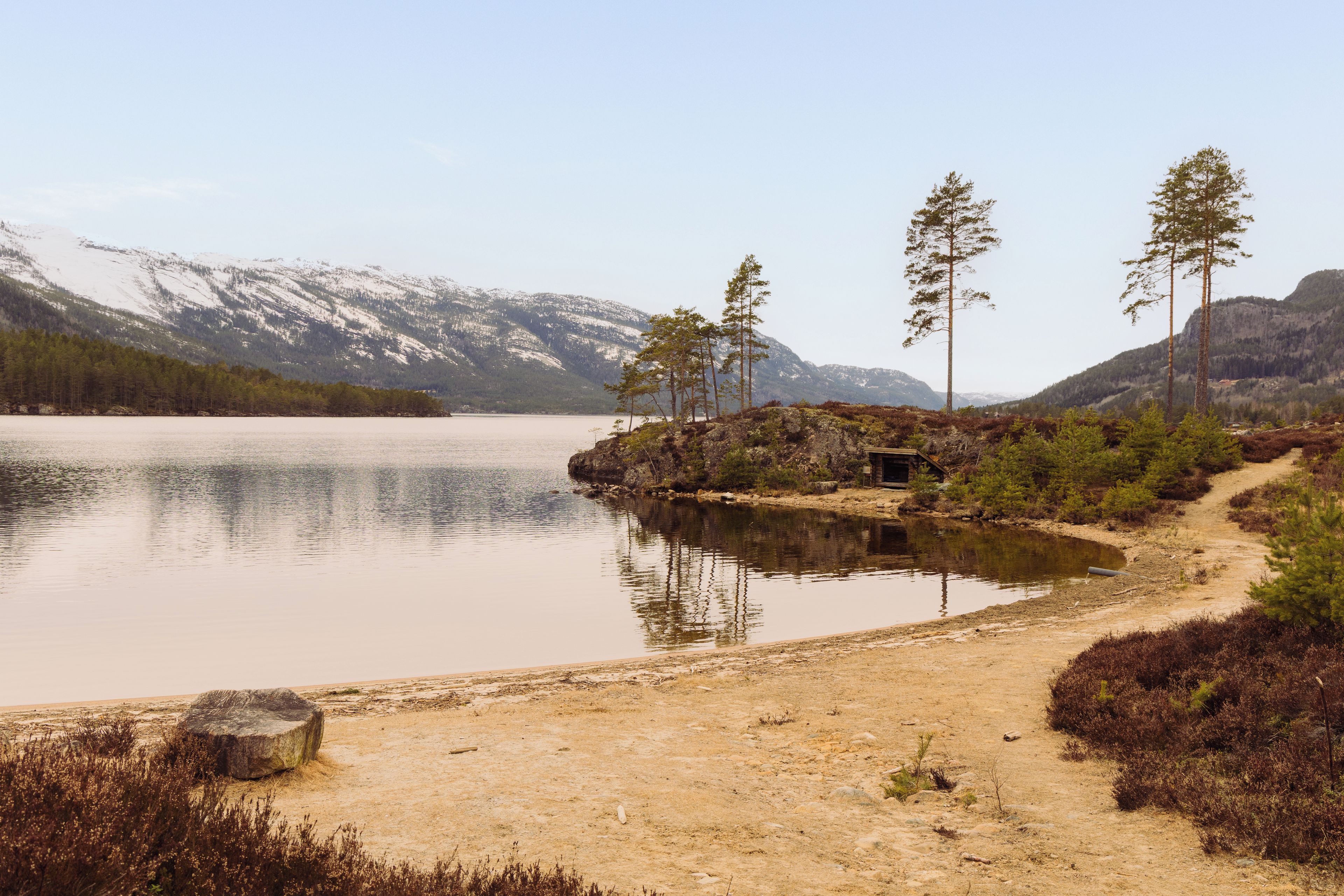 A natural landscape with a lake, mountains, and a dirt path.