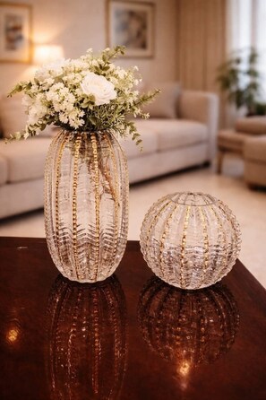 Eine Glasvase mit Blumenarrangement und einem kleinen Glasornament auf einer spiegelnden Oberfläche.