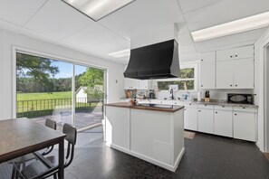 Eine moderne Küche mit weißen Schränken, einer großen Kochinsel und einer Schiebetür zu einer Terrasse.