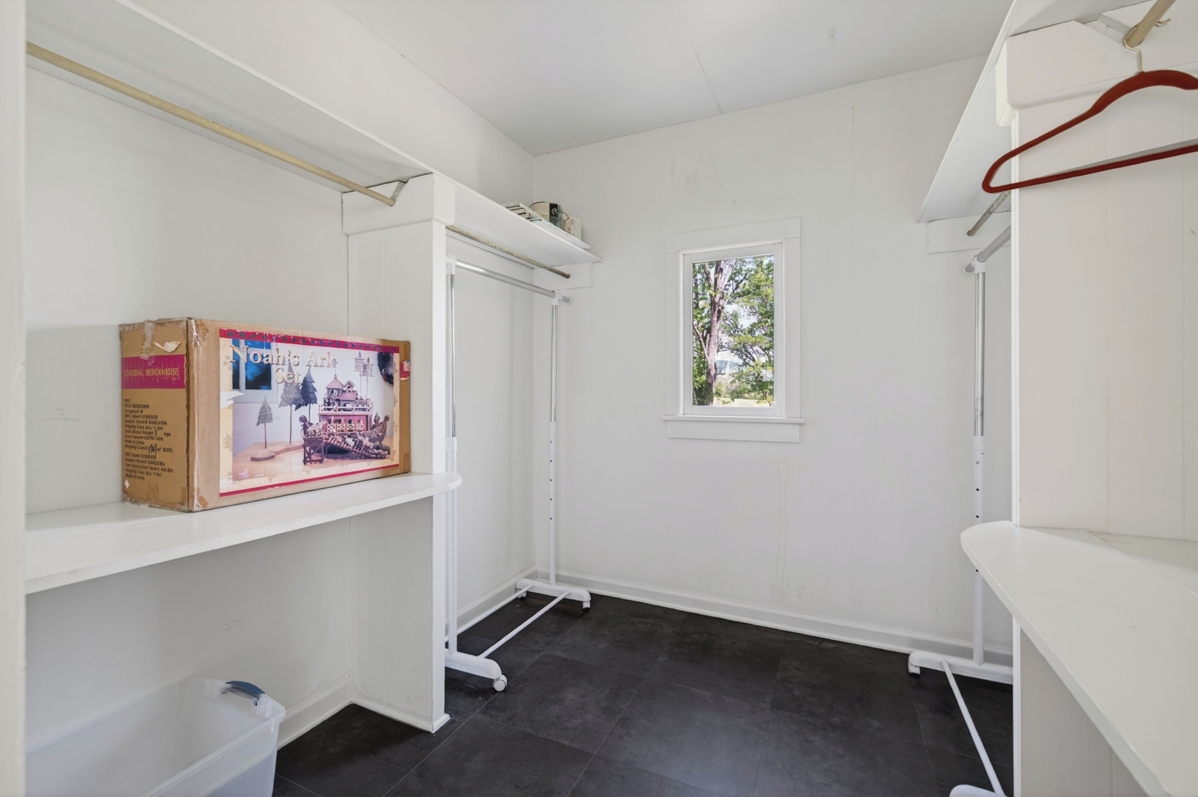A room with white walls, a window with a view, a white shelf, and a cardboard box.