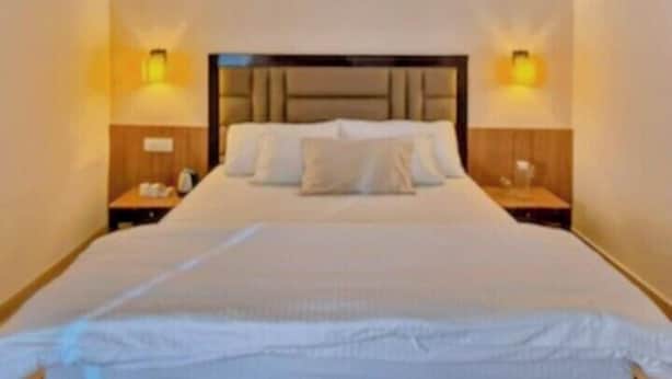 A hotel room with a large bed, two bedside tables, and wall-mounted lamps. - Hotel City Palace (Ranchi)