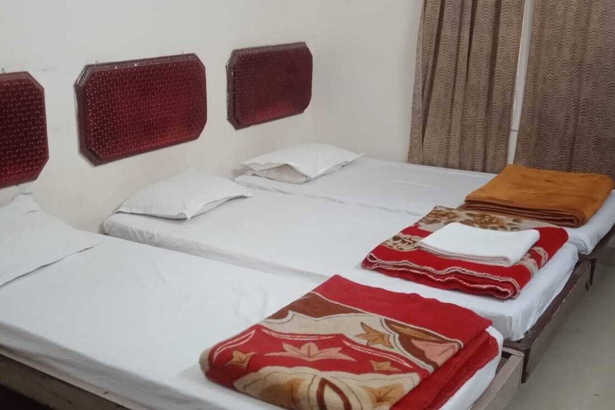 Una habitación con dos camas individuales, cada una con colchón y almohadas blancas, y una manta roja estampada en la cama de la derecha.