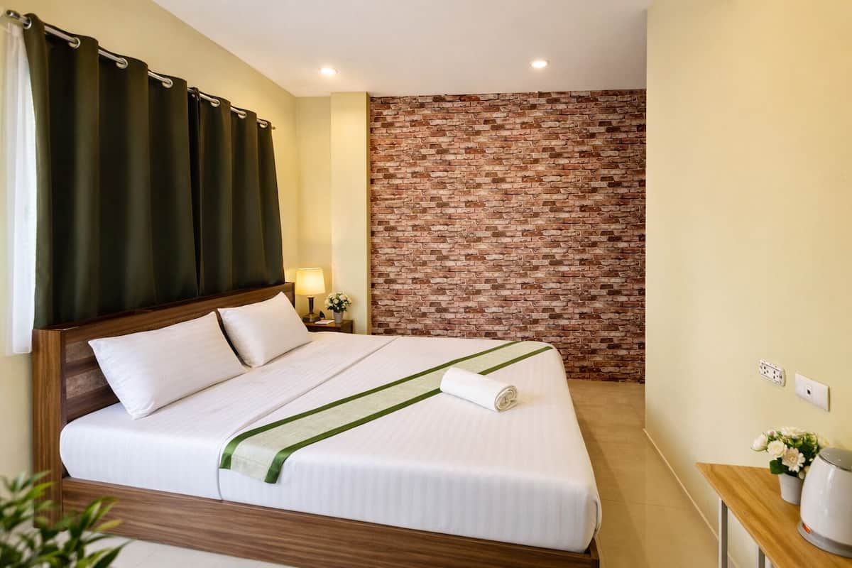 Habitación de hotel con cama, pared de ladrillo, mesita de noche con lámpara y ventana con cortinas.
