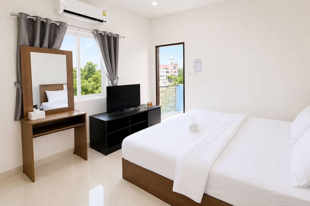 Una habitación de hotel con cama, televisor, escritorio y ventana con cortinas.