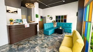 Een receptie met een balie, een blauwe bank, een gele fauteuil en een kleurrijk raam.