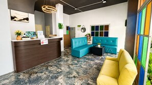Un'area reception con un banco, un divano blu, una poltrona gialla e una finestra colorata.