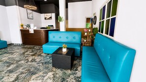 A reception area with a blue sofa, a small table with a vase, and a reception desk. - Luxus Guesthouse Patong (Patong)