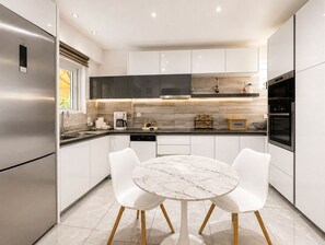 A modern kitchen with white cabinetry, a marble dining table, and stainless steel appliances. - Chalandri Spacious 4BR 3-Level Maisonette by ΜΡS (Chalandri)
