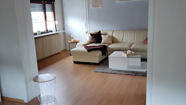 A living room with a beige sofa, a small round table, and a cat. - Cozy vacation apartment in Herdorf (Herdorf)