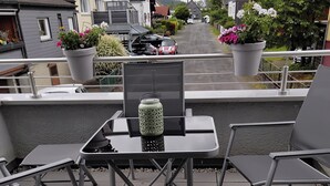 An outdoor patio with a table and chairs, a potted plant, and a view of the street. - Cozy vacation apartment in Herdorf (Herdorf)