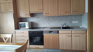 A kitchen with wooden cabinets, a microwave, a sink, and a stove. - Cozy vacation apartment in Herdorf (Herdorf)