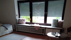 A room with a wooden floor, a bed with pillows, a small round table, and a window with blinds. - Cozy vacation apartment in Herdorf (Herdorf)