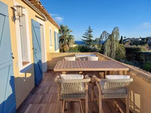 A wooden deck with a table and chairs, a blue door, and a view of the sea and hills. - Villa Jardin Azur - Pool - Gulf of St-Tropez (Roquebrune-sur-Argens)