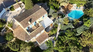 An aerial view of a residential property with a swimming pool, multiple terraces, and lush greenery.
