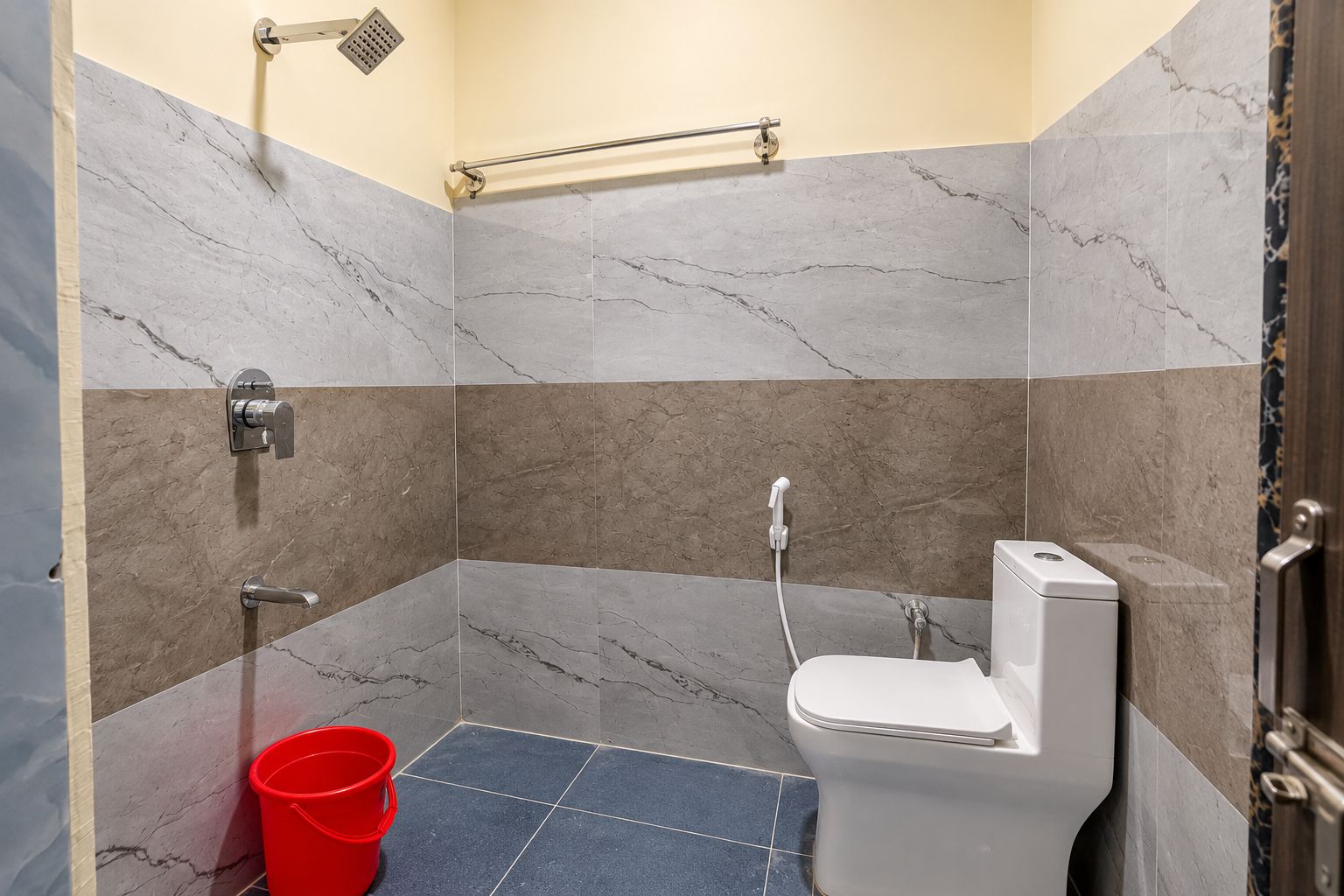 A bathroom with a shower, toilet, and a red bucket.