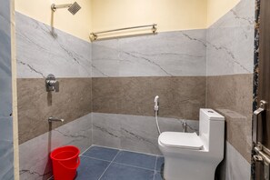 Un baño con ducha, inodoro y un cubo rojo.
