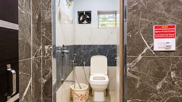 A bathroom with a glass-enclosed shower, a toilet, and a bucket. A notice is visible on the wall.