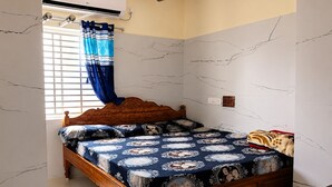 A bedroom with a wooden bed, patterned bedspread, a window with curtains, and a wall with a marble-like design. - SVS Grands (Atreyapuram)