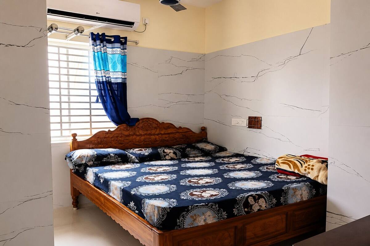 Quarto com cama de madeira, colcha estampada, janela com cortinas e parede com efeito marmorizado.