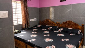A bedroom with a bed, a ceiling fan, an air conditioning unit, a window with curtains, and a wall-mounted picture. - SVS Grands (Atreyapuram)