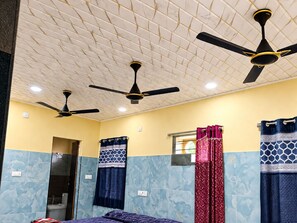 A room with three ceiling fans, a bed, a shower, and a window with curtains. - SVS Grands (Atreyapuram)