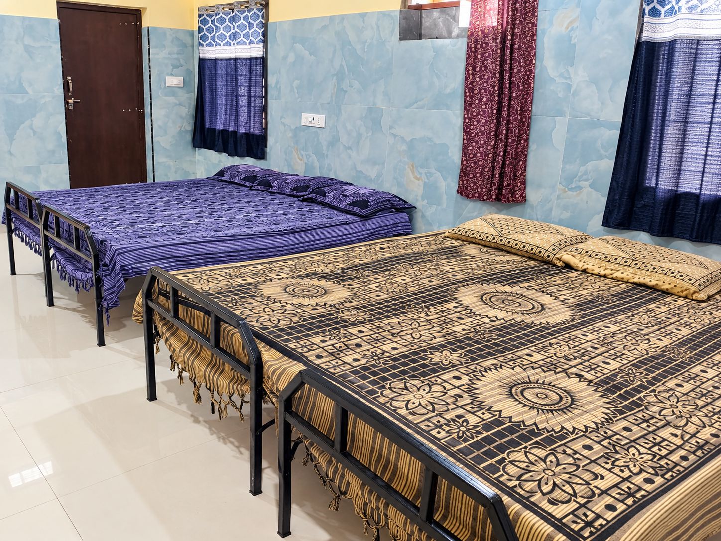 A room with two beds, a door, and patterned curtains.