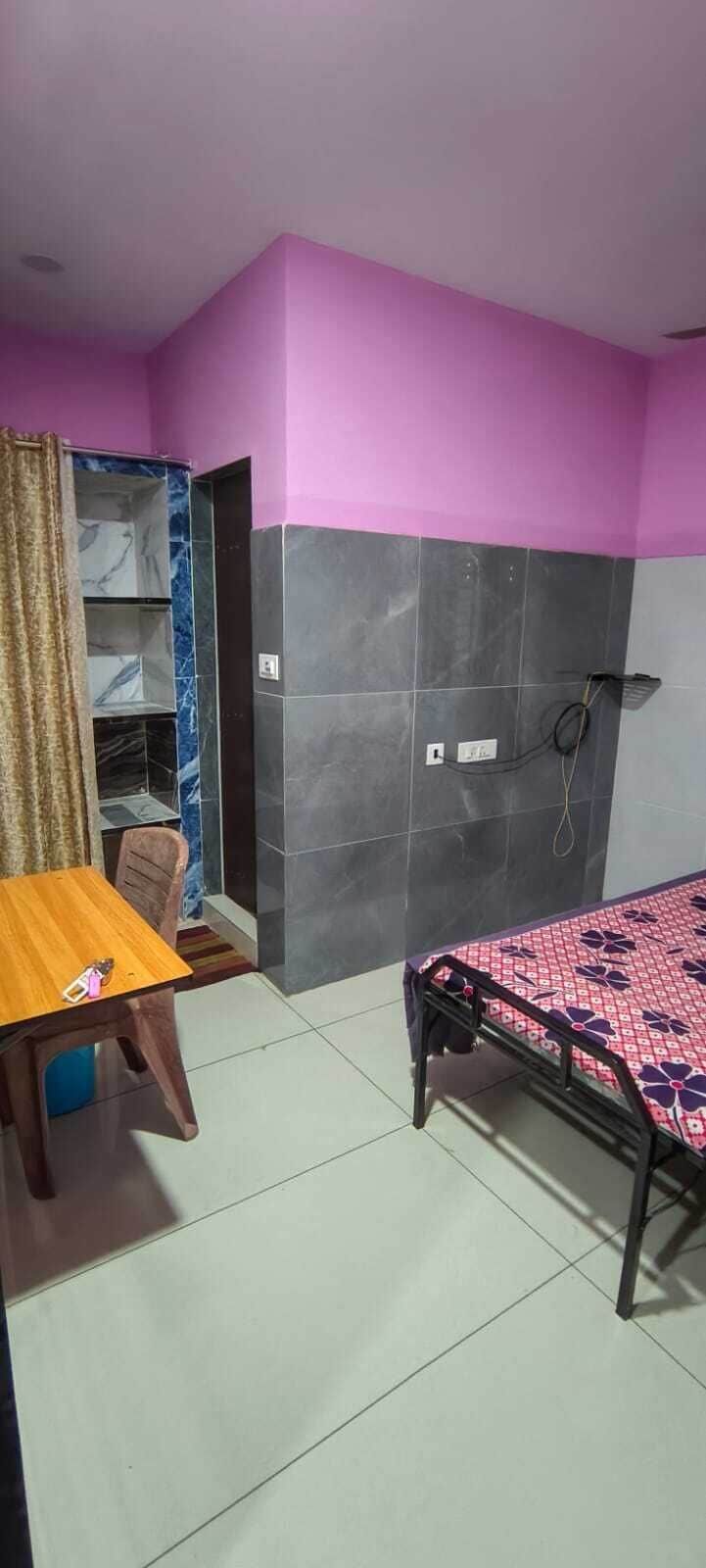 Une pièce comprenant un lit, une table et une chaise. On y trouve une armoire avec un miroir et une étagère. Les murs sont peints en deux couleurs.