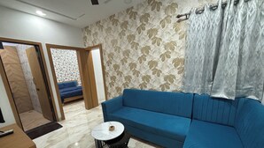 Un salon avec un canapé bleu, une petite table ronde, un papier peint à motifs et une porte donnant sur une autre pièce.