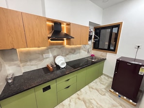Una cocina con gabinetes verdes, encimera negra, un lavabo y un refrigerador Haier.