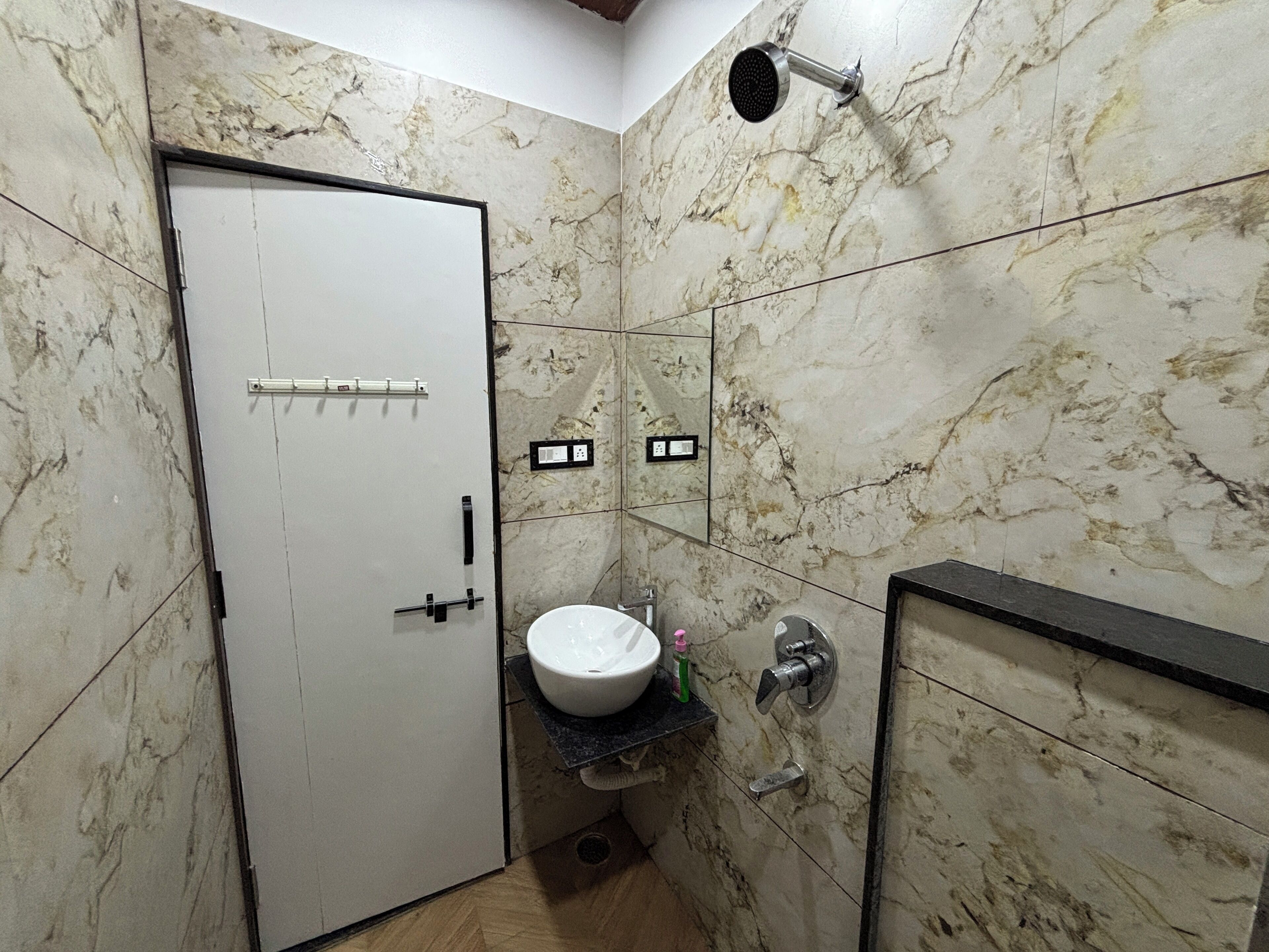 Een badkamer met een witte deur, een wastafel, een spiegel en een douche.