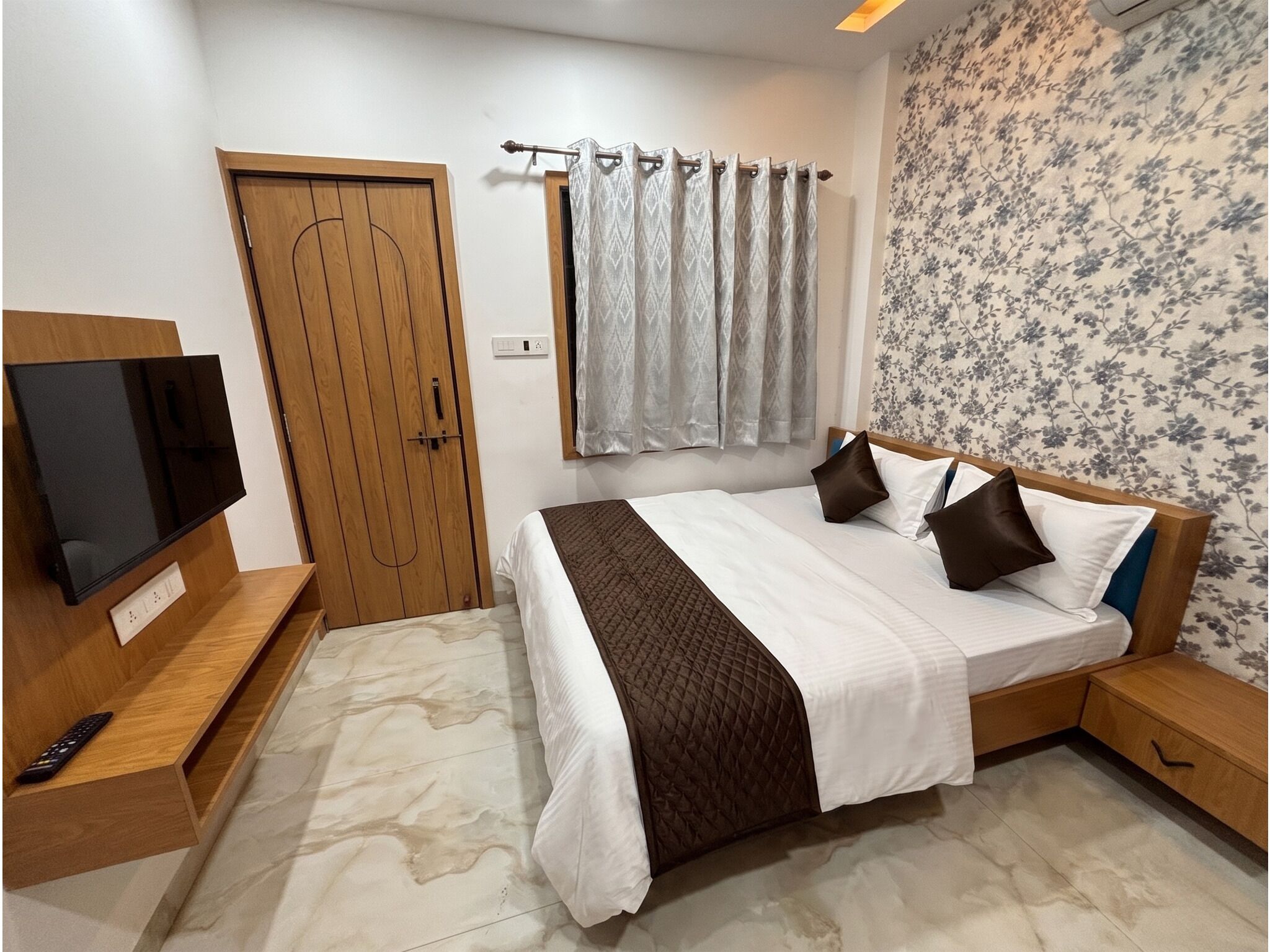 A bedroom with a bed, a TV, a wardrobe, and a window with curtains.