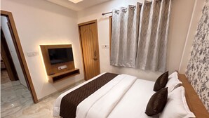 Une chambre d’hôtel avec un lit, un téléviseur fixé au mur, une porte en bois et un rideau.