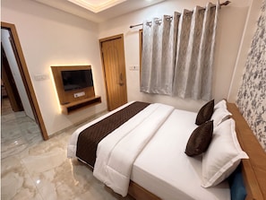 Habitación de hotel con cama, televisor montado en la pared, puerta de madera y cortina.