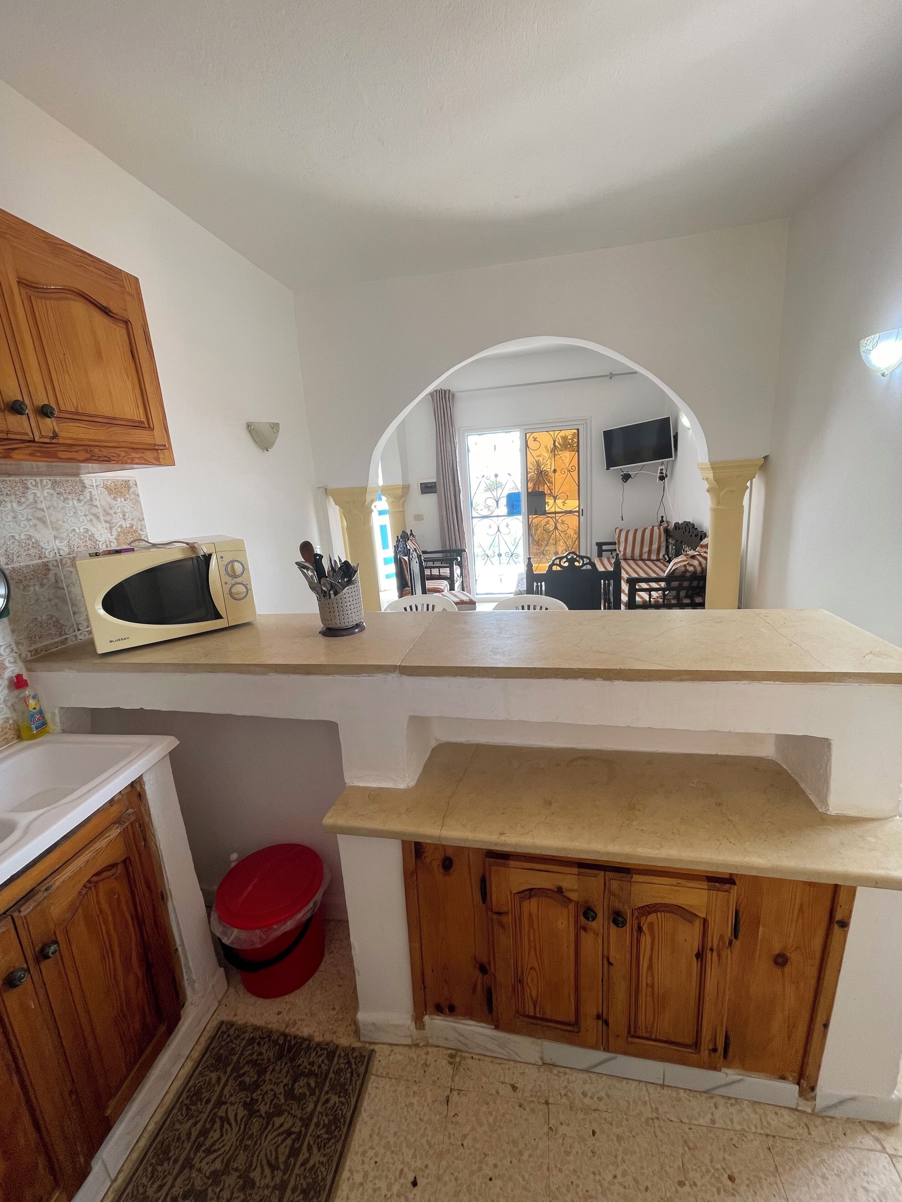A kitchen with wooden cabinets, a microwave, and a red trash bin.