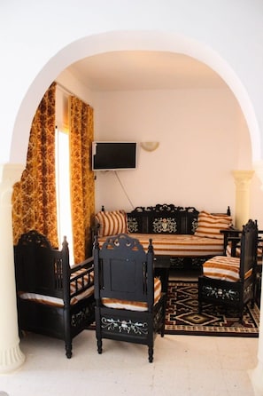 Une piÚce comprenant un canapé, deux fauteuils, un téléviseur et un tapis à motifs.