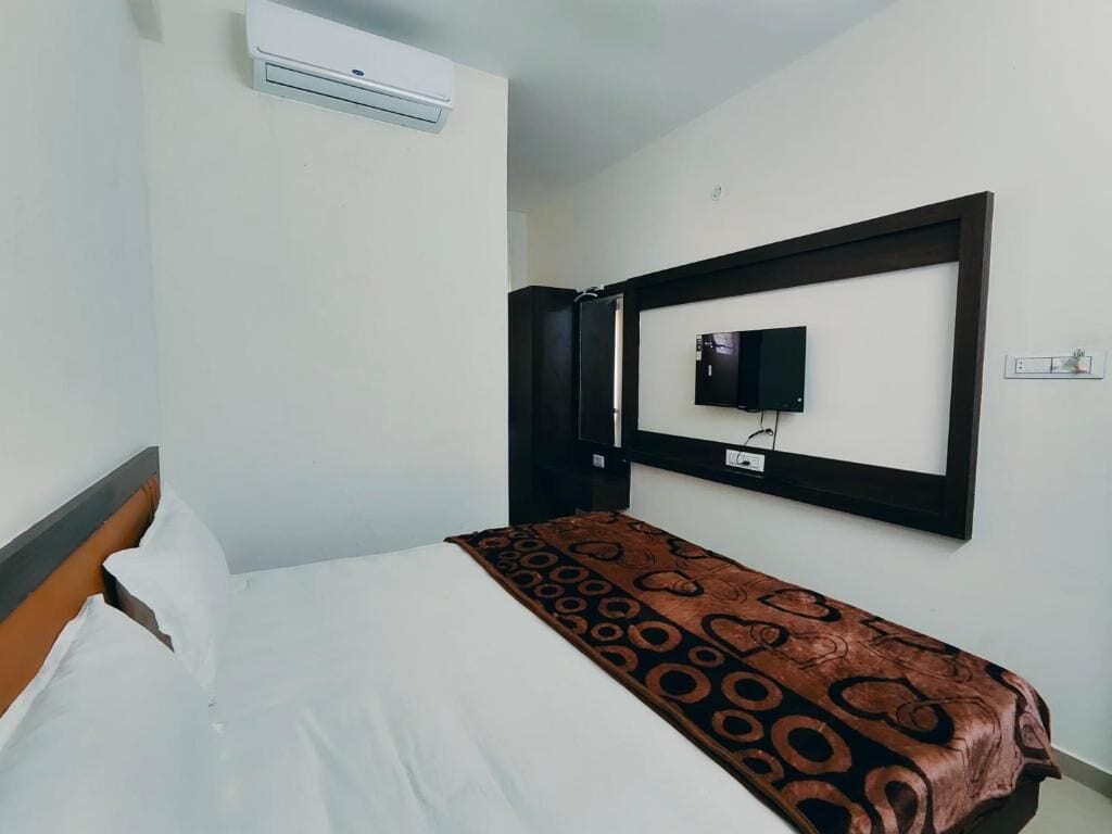 A hotel room with a bed, a television mounted on the wall, and an air conditioning unit above the bed.