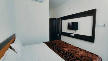 A hotel room with a bed, a television mounted on the wall, and an air conditioning unit above the bed.