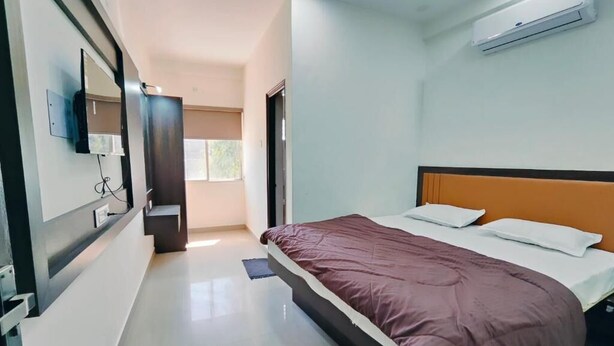 A bedroom with a bed, a mirror, an air conditioner, and a door leading to another room.